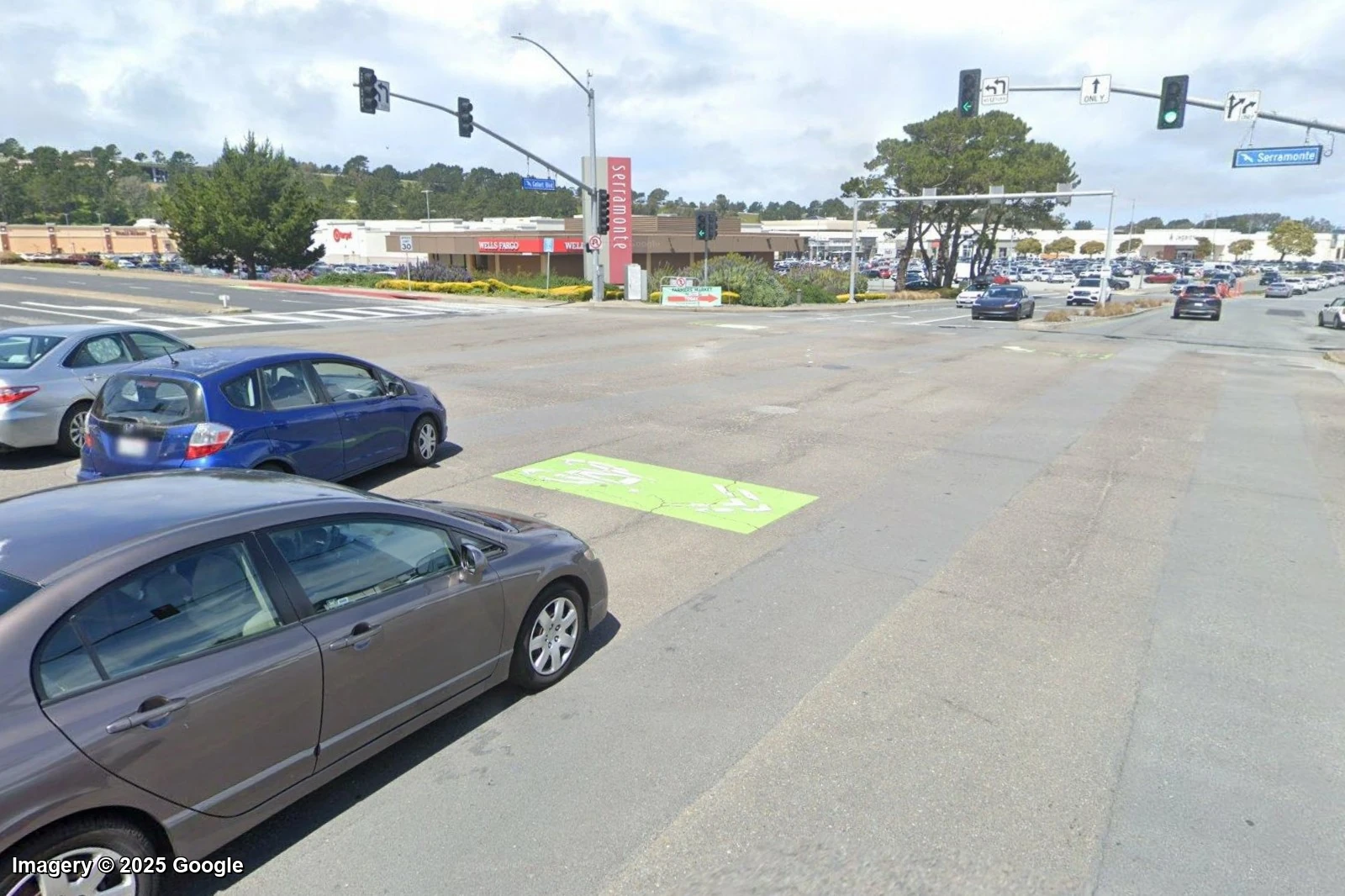 A wide multi-lane arterial outside the Serramonte mall in Daly City, with parking lots and no shade, the kind of place Walk Grade rates an F